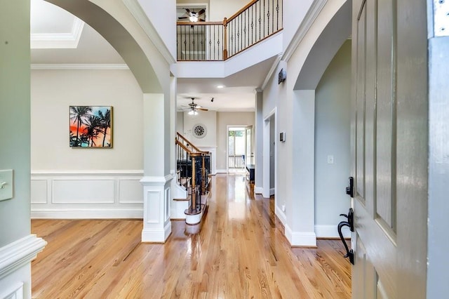 foyer featuring arched walkways, light wood-style flooring, stairs, a ceiling fan, and ornamental molding