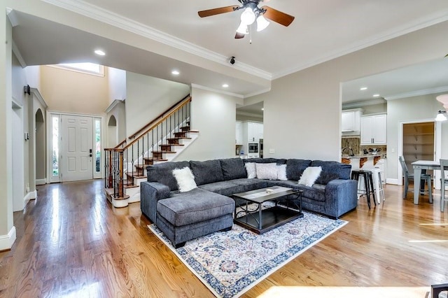 living area with light wood-type flooring, a ceiling fan, stairs, and ornamental molding