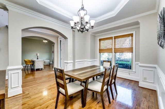 dining space with crown molding, arched walkways, a wainscoted wall, a notable chandelier, and light wood-style flooring