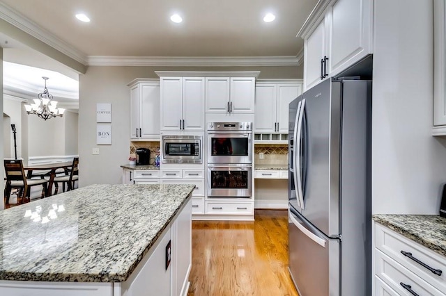 kitchen featuring crown molding, decorative backsplash, white cabinets, a chandelier, and stainless steel appliances