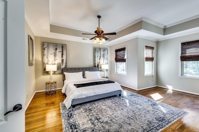 bedroom featuring a tray ceiling, ornamental molding, baseboards, and wood finished floors