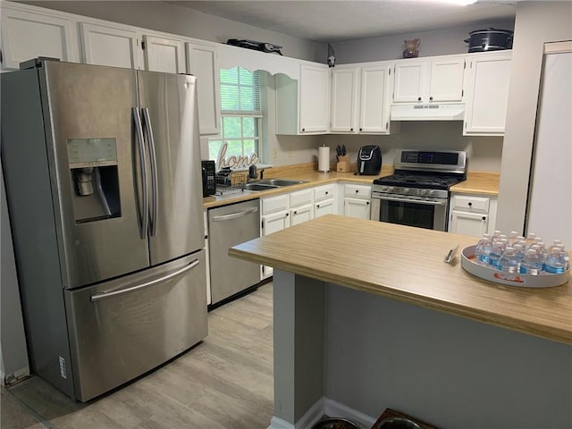 kitchen with a sink, under cabinet range hood, light wood-style flooring, white cabinetry, and appliances with stainless steel finishes