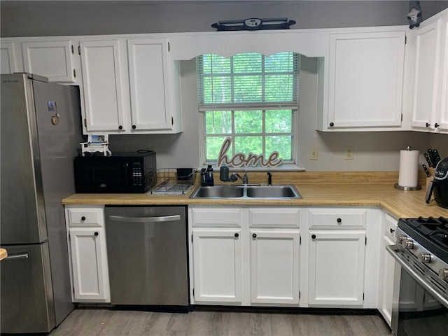 kitchen with light wood-style flooring, white cabinets, a sink, stainless steel appliances, and light countertops