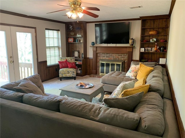 living room with ornamental molding, a ceiling fan, carpet, and a brick fireplace