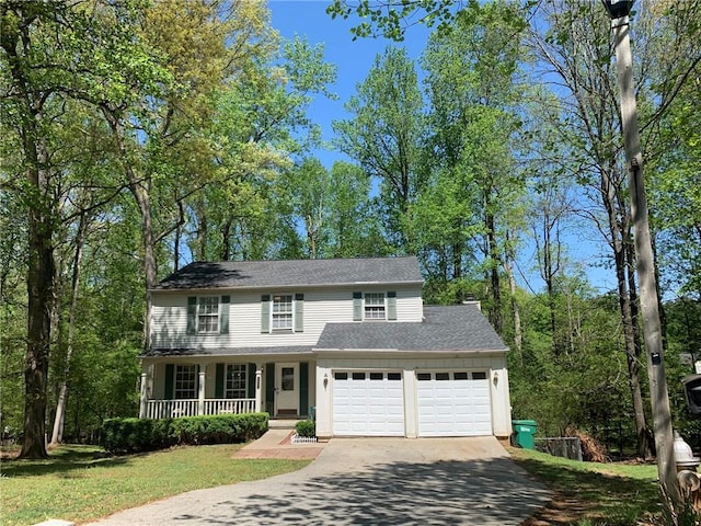 traditional-style home featuring a front yard, a shingled roof, covered porch, aphalt driveway, and an attached garage