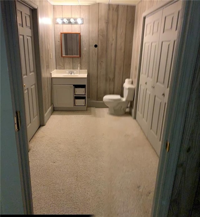 bathroom featuring wood walls, toilet, and vanity