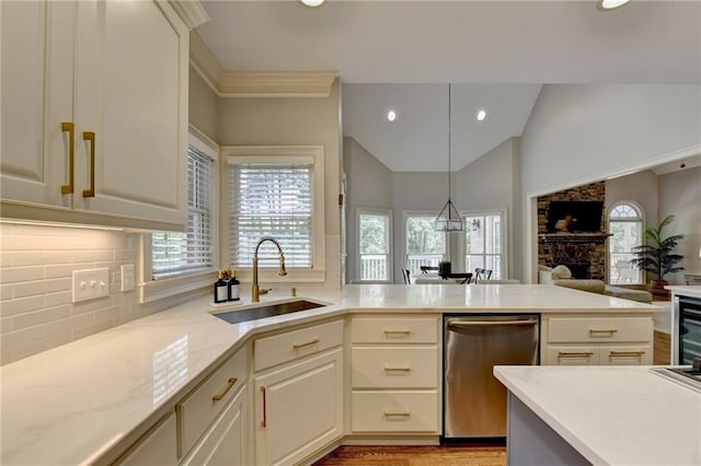 kitchen with light wood-type flooring, stainless steel dishwasher, a stone fireplace, sink, and vaulted ceiling