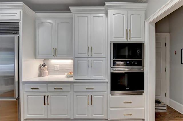 kitchen with built in appliances, tasteful backsplash, hardwood / wood-style flooring, and white cabinetry