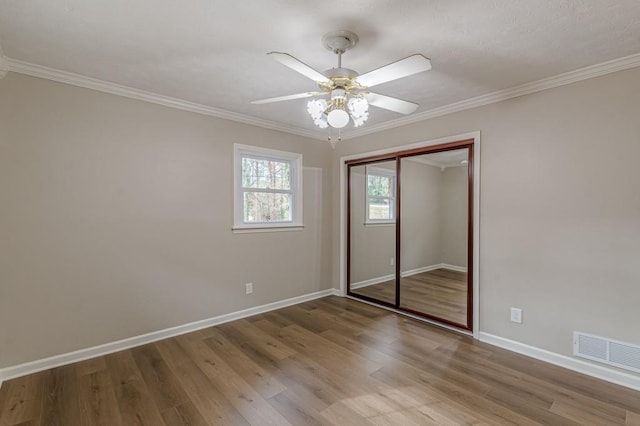 unfurnished bedroom with hardwood / wood-style flooring, ornamental molding, ceiling fan, and a closet
