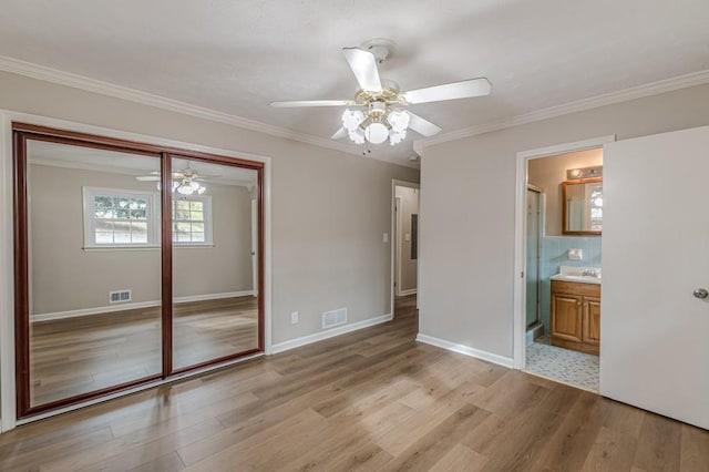 unfurnished bedroom featuring crown molding, ceiling fan, connected bathroom, a closet, and light wood-type flooring