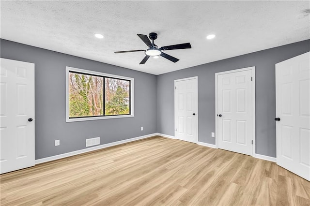 unfurnished bedroom featuring ceiling fan, two closets, a textured ceiling, and light wood-type flooring