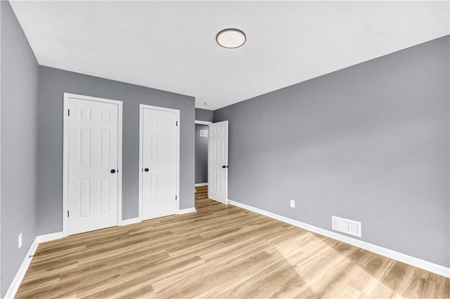 unfurnished bedroom featuring two closets and light hardwood / wood-style flooring