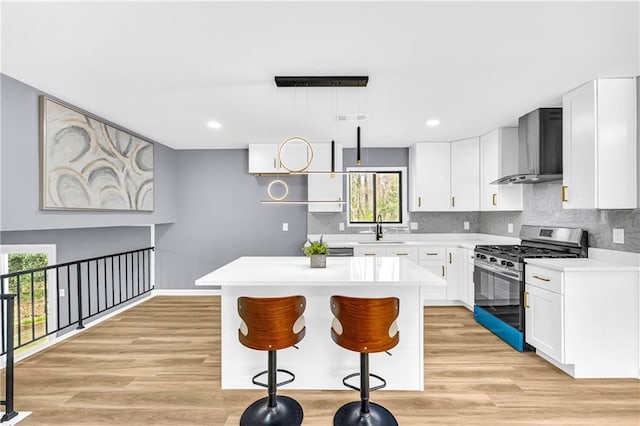 kitchen with white cabinetry, gas range, a center island, and wall chimney range hood