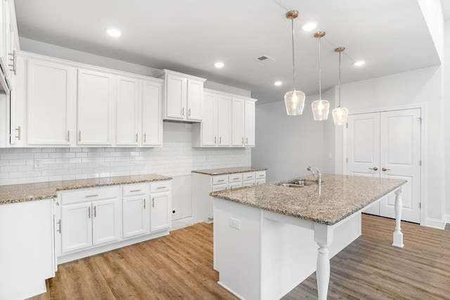 kitchen with a sink, light stone counters, an island with sink, light wood finished floors, and white cabinetry
