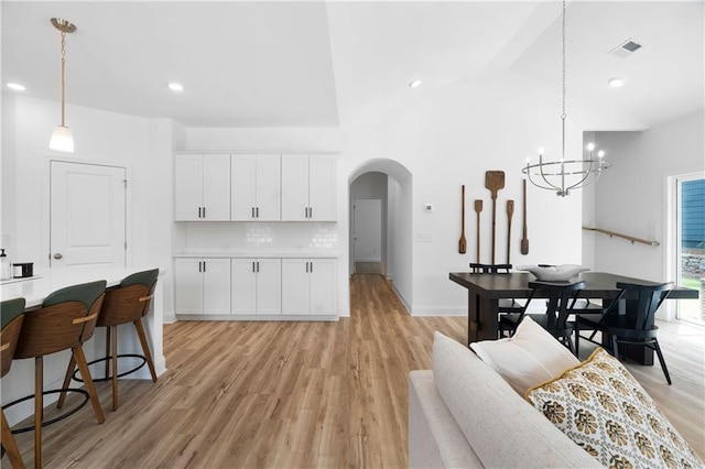 living area with visible vents, a notable chandelier, arched walkways, light wood-style floors, and a towering ceiling