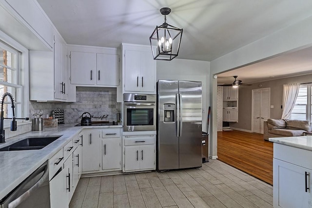 kitchen with tasteful backsplash, light wood-style floors, white cabinets, stainless steel appliances, and a sink