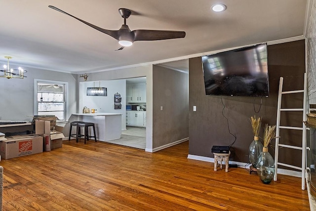 living room with baseboards, wood finished floors, ornamental molding, and ceiling fan with notable chandelier