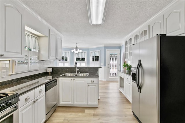 kitchen featuring a textured ceiling, a sink, a peninsula, a notable chandelier, and stainless steel appliances