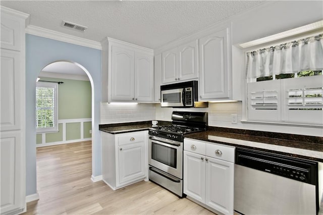 kitchen with visible vents, dark countertops, white cabinets, light wood-style floors, and stainless steel appliances