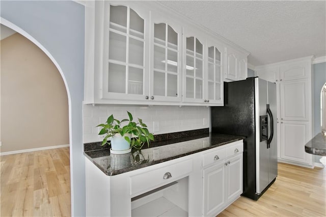 kitchen with backsplash, arched walkways, white cabinets, dark stone countertops, and glass insert cabinets