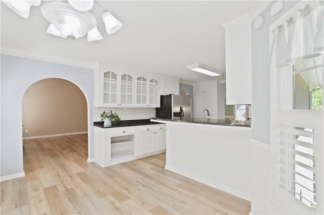 kitchen with dark countertops, arched walkways, white cabinetry, stainless steel refrigerator with ice dispenser, and glass insert cabinets