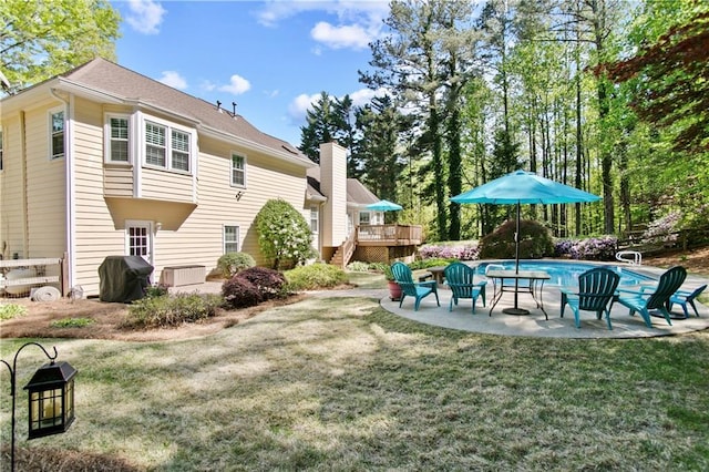back of property featuring a lawn, a deck, an outdoor pool, and a patio area