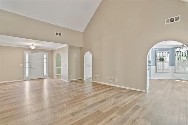 unfurnished living room featuring visible vents, arched walkways, light wood finished floors, and high vaulted ceiling
