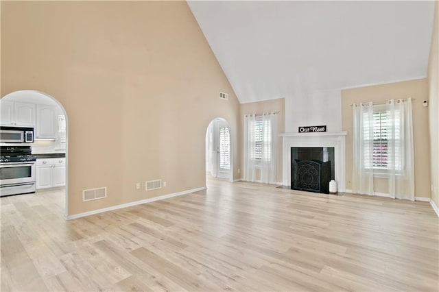 unfurnished living room featuring visible vents, arched walkways, light wood-style floors, and high vaulted ceiling