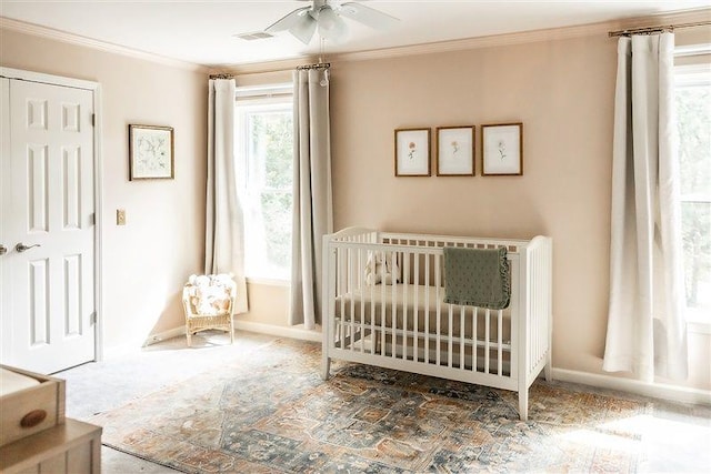 carpeted bedroom featuring ornamental molding, a nursery area, and ceiling fan