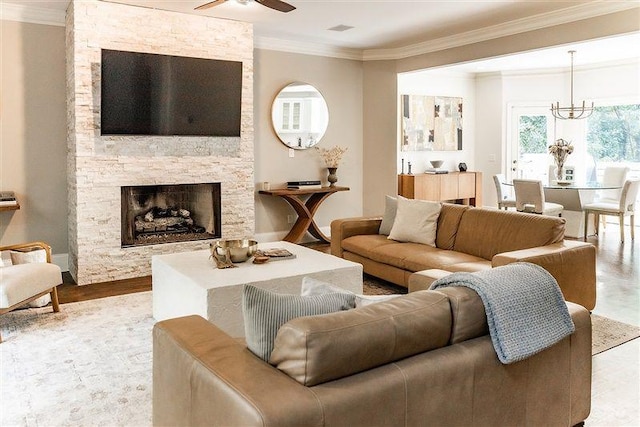 living room with crown molding, a stone fireplace, and ceiling fan with notable chandelier