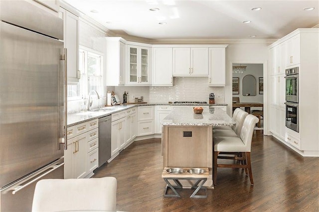 kitchen with white cabinetry, light stone countertops, stainless steel appliances, and a center island