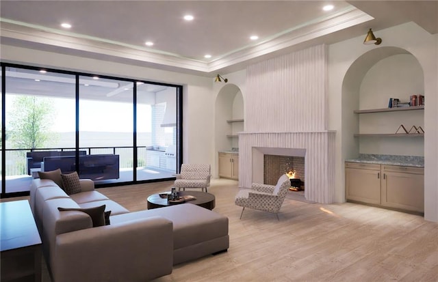 living area with light wood-type flooring, a raised ceiling, crown molding, a fireplace, and recessed lighting
