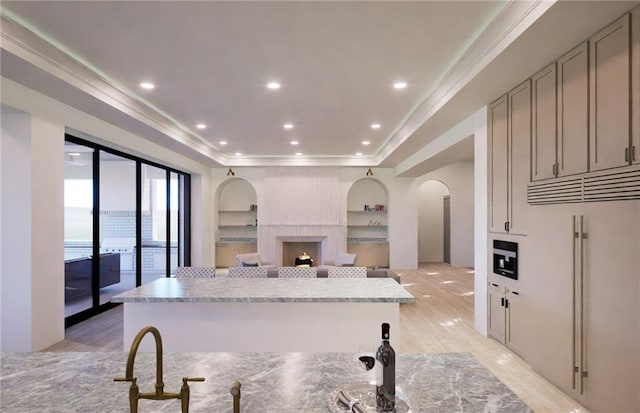 kitchen with gray cabinetry, light wood-style flooring, a kitchen island, a tray ceiling, and arched walkways