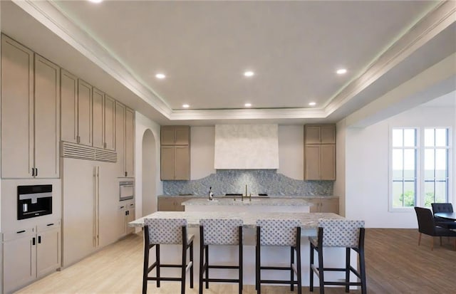 kitchen with built in fridge, a raised ceiling, backsplash, arched walkways, and light wood-style flooring