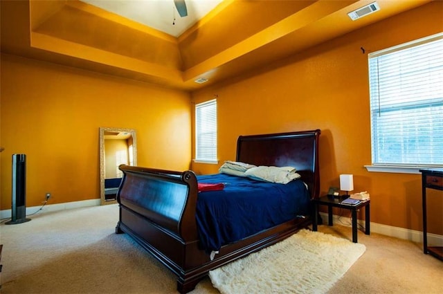 bedroom with a tray ceiling, ceiling fan, and light carpet