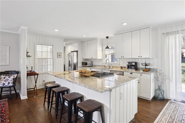 kitchen with stainless steel appliances, a kitchen island, pendant lighting, and white cabinets