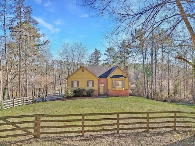 view of front of property featuring a forest view, a fenced front yard, a chimney, a front yard, and brick siding