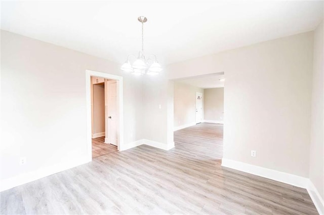 spare room featuring a notable chandelier and light wood-type flooring