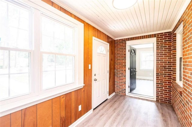 interior space with light hardwood / wood-style floors, wooden ceiling, brick wall, and ornamental molding