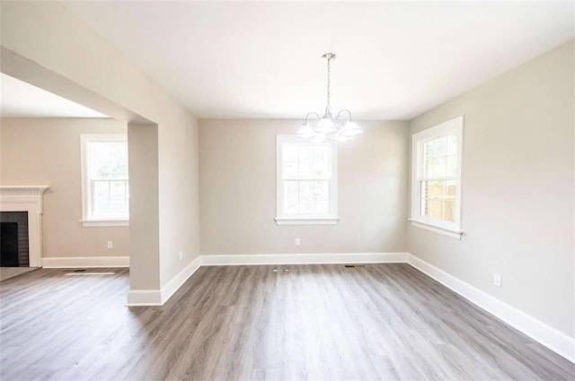 unfurnished dining area featuring a brick fireplace, an inviting chandelier, and light hardwood / wood-style floors