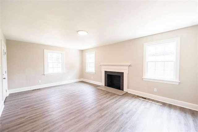 unfurnished living room featuring wood-type flooring and a brick fireplace