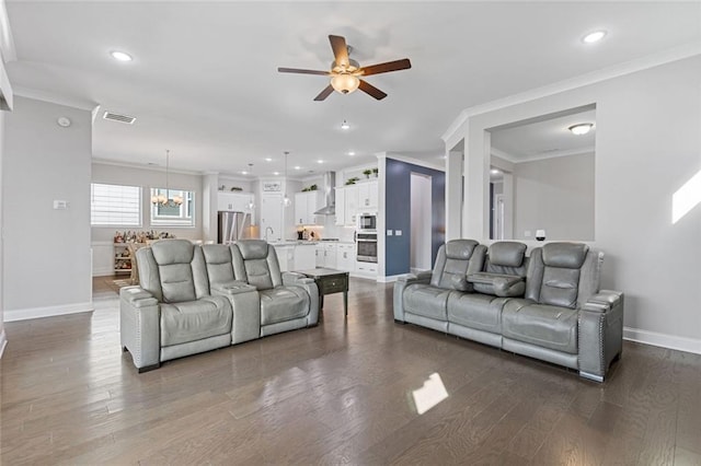 living area featuring dark wood-style flooring, crown molding, visible vents, baseboards, and ceiling fan with notable chandelier