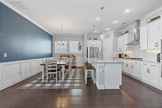 kitchen featuring dark wood finished floors, stainless steel appliances, white cabinets, a sink, and wall chimney exhaust hood
