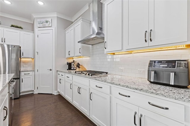 kitchen featuring wall chimney range hood, appliances with stainless steel finishes, white cabinets, and crown molding
