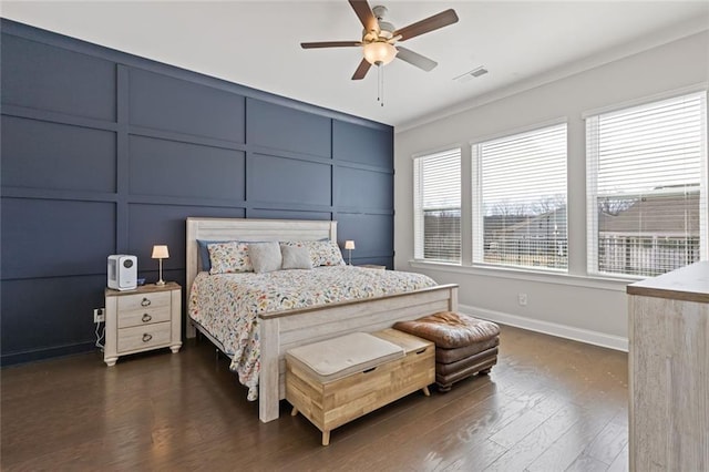 bedroom with a decorative wall, dark wood-style flooring, visible vents, baseboards, and crown molding