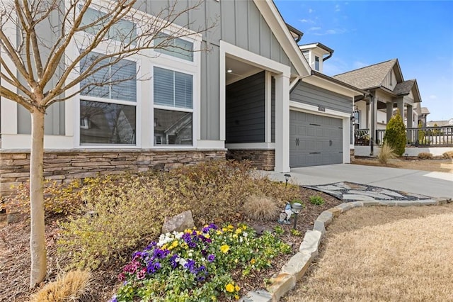 view of side of home featuring a garage, stone siding, board and batten siding, and concrete driveway
