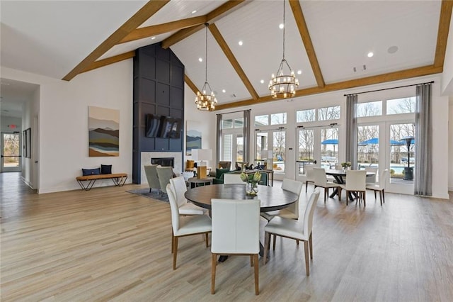 dining space featuring light wood-style floors, a fireplace, high vaulted ceiling, and an inviting chandelier