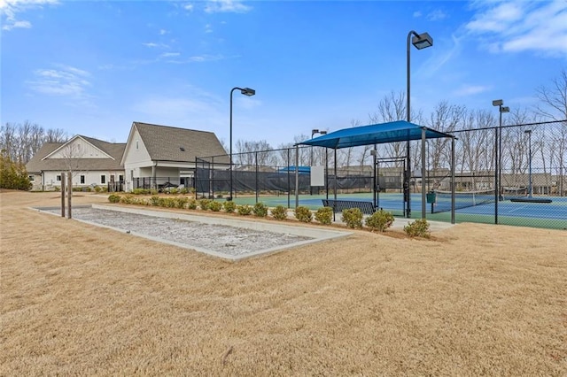 view of community featuring a yard, a tennis court, and fence