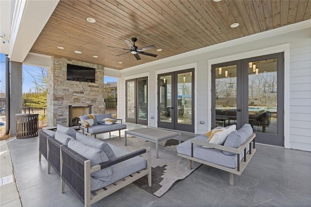 view of patio featuring a ceiling fan, french doors, fence, and an outdoor living space with a fireplace