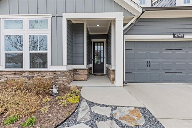 entrance to property featuring a garage, concrete driveway, board and batten siding, and stone siding